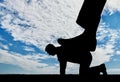 Silhouette of a large leg pressing on a man who fell on all fours.