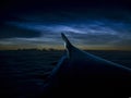 Silhouette of the left wing at cruising altitude above the clouds at night, against the backdrop of noctilucent clouds. Royalty Free Stock Photo