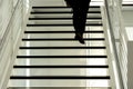 Silhouette of legs and feet of a man climbing up the black steps of a modern open staircase