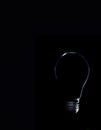 Silhouette of a light bulb on a black background, subtle light outlining an extinguished light bulb, copy space