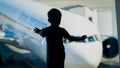 Silhouette of little boy looking on big airplane through big window in airport terminal Royalty Free Stock Photo