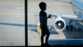 Silhouette of little boy standing at big window in airport terminal and looking on airplane at gate