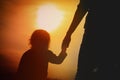 Silhouette of little girl holding parent hand at sunset