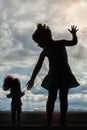 Silhouette of a little girl standing on the window with her favorite doll on the background of blue sky, clouds Royalty Free Stock Photo