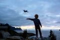 Silhouette of little toddler child, catching drone in the air, standing on a rock, splendid beautiful mountain landscape from