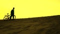 Silhouette of lonely biker walking with his bike along sand dune, yellow sunset colors Royalty Free Stock Photo