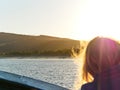 Silhouette of a long-haired girl at sunset, looking at the coastal forest from a boat on sea