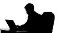 Silhouette of male analyst typing on laptop at office desk, business person