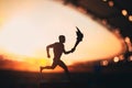 Silhouette of Male Athlete Carrying the Torch Relay, Illuminating the Modern Track and Field Stadium. A Captivating Snapshot for Royalty Free Stock Photo
