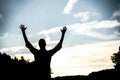 Silhouette of a male with his hands up towards the sky with a blurred background