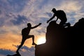 Silhouette of a male mountaineer working in a team with a partner, giving him a helping hand