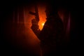 Silhouette of man with assault rifle ready to attack on dark toned foggy background or dangerous bandit in black wearing balaclava