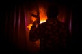 Silhouette of man with assault rifle ready to attack on dark toned foggy background or dangerous bandit in black wearing balaclava