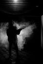 Silhouette of man with assault rifle ready to attack on dark toned foggy background or dangerous bandit in black wearing balaclava