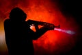 Silhouette of man with assault rifle ready to attack on dark toned foggy background or dangerous bandit in black wearing balaclava