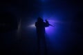 Silhouette of man with assault rifle ready to attack on dark toned foggy background or dangerous bandit in black wearing balaclava