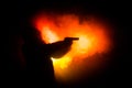 Silhouette of man with assault rifle ready to attack on dark toned foggy background or dangerous bandit in black wearing balaclava