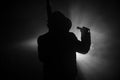 Silhouette of man with assault rifle ready to attack on dark toned foggy background or dangerous bandit in black wearing balaclava