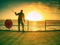 Silhouette of man with backpack on the pier on the calm sea