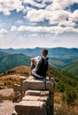 Silhouette of man with backpack sitting with his back to the photographer on the big rock and looking at the panorama of