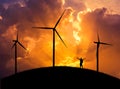 Silhouette the man backpacker standing raised up arms celebrate on the hill with wind turbines in sunset. Royalty Free Stock Photo