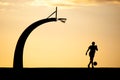 Silhouette of a man with a basketball hoop and ball against a backdrop of an orange sky at sunset