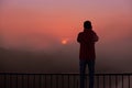 A silhouette of a man on a bridge over the river that photographs a sunrise on a foggy morning