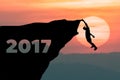 Silhouette Man climbs into cliff to the goal setting of word Happy New Year 2017 with sunset in background.