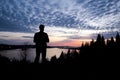 Silhouette of a man controlling a drone that is in the background with the sun setting over downtown Vancouver.