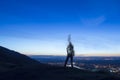 A silhouette of a man disappearing and turning into smoke. Standing on a hill. Lookng out on city lights just before sunrise