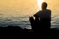 Silhouette of man and dog sitting together at the seaside and looking at the sunrise Royalty Free Stock Photo
