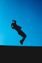 Silhouette of a man doing parkour with the blue sky in the background. Extreme somersault