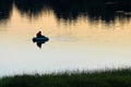 A silhouette of man fly fishing on a quiet summer evening