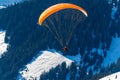 Silhouette of a man flying a hang glider in the mountains of Austria in the Zell am See area. Below the man is a snowy valley and