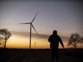 Silhouette of a man goes to sunset in the direction of wind turbines Royalty Free Stock Photo