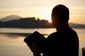 Silhouette of a man holding the bible surrounded by hills and the sea during the sunset Royalty Free Stock Photo