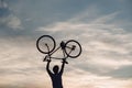 Silhouette of man holding bike above head.