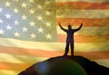 Silhouette of a man holding his hands up on the top of a mountain, against the background of the sky of the flag of America, USA. Royalty Free Stock Photo