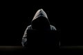 Silhouette of a man in a hood on a black background, his face is not visible, he sits at the computer. The concept of a criminal, Royalty Free Stock Photo