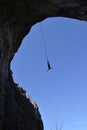 Silhouette of a man jumping in a cave hanging high on a cord