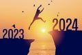 Silhouette man jumping between cliff with number 2023 to 2024 and birds flying at tropical sunset beach. Freedom challenge and