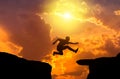 Silhouette the man jumping through the gap over rock cliff between mountain on sunset Royalty Free Stock Photo