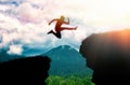 The silhouette of a man jumping over a chasm between rocks. In the background, the ocean and the sky. The concept of