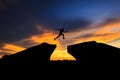 Silhouette of man jumping over cliff on sunset background