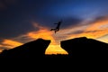 Silhouette of man jumping over cliff on sunset background, Royalty Free Stock Photo