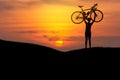 Silhouette the man lifting bicycle above his head on the meadow with sunset Royalty Free Stock Photo