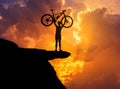 Silhouette the man lifting mountain bicycle above his head on top of cliff mountain with sunset Royalty Free Stock Photo