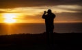 Silhouette of a man looking out over the ocean taking a cell phone picture at a sunset Royalty Free Stock Photo