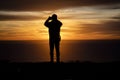 Silhouette of a man looking out over the ocean taking a cell phone picture at a sunset Royalty Free Stock Photo