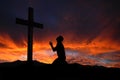 Silhouette of man praying to a cross with heavenly cloudscape sunset Royalty Free Stock Photo